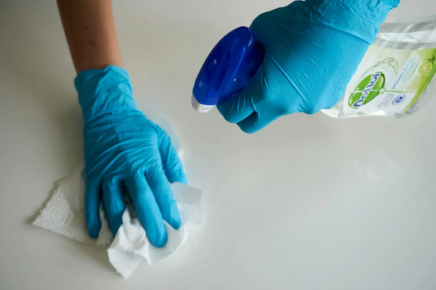 A gloved hand wiping down a kitchen bench with a cloth
