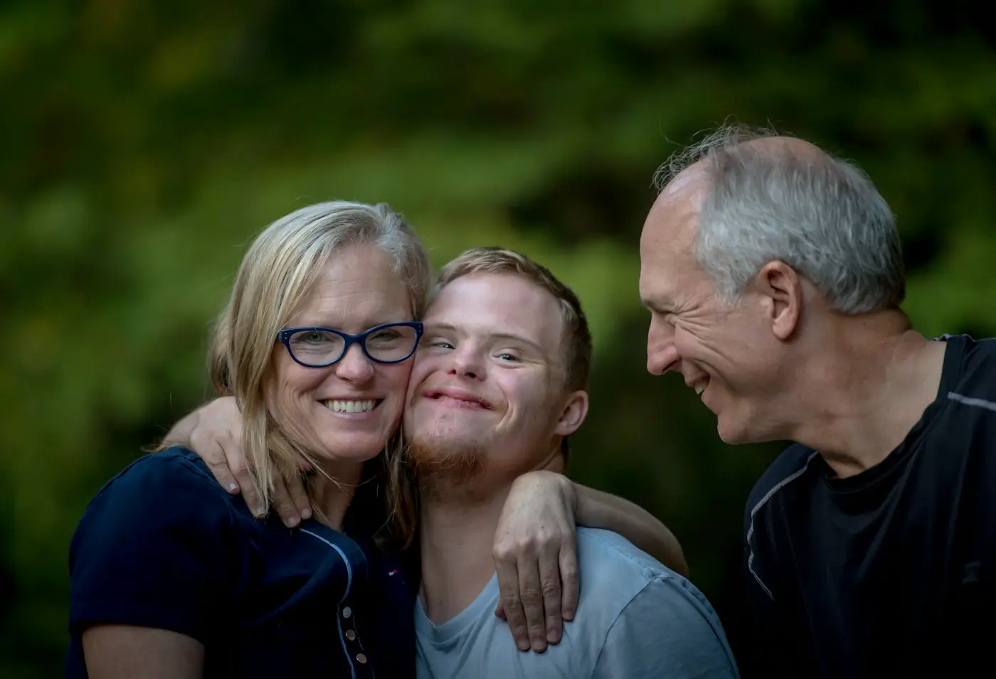 Young man with Down syndrome being hugged by two older adults outdoors