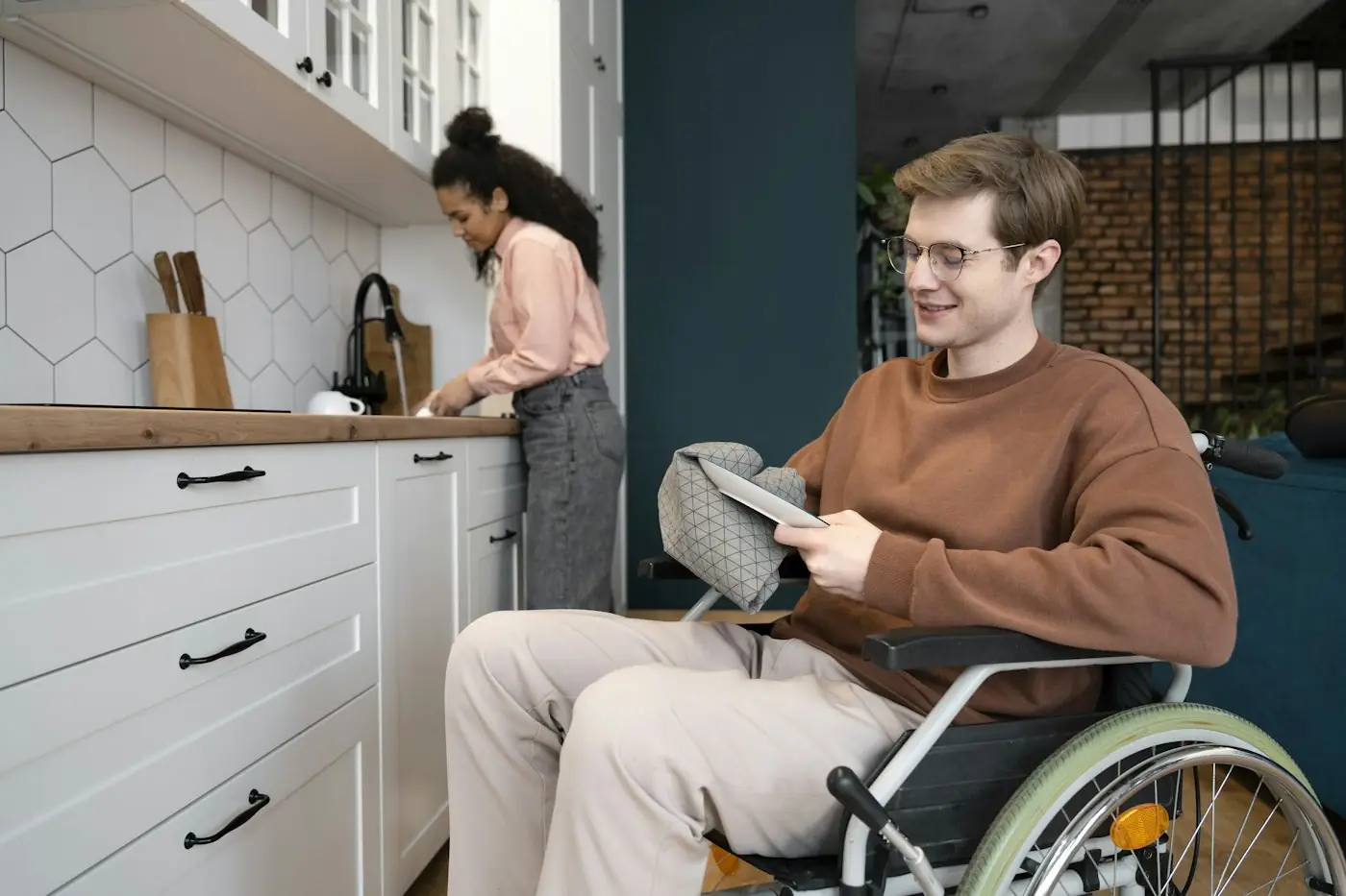 A young man using a wheelchair in a modern kitchen while a woman cooks behind him