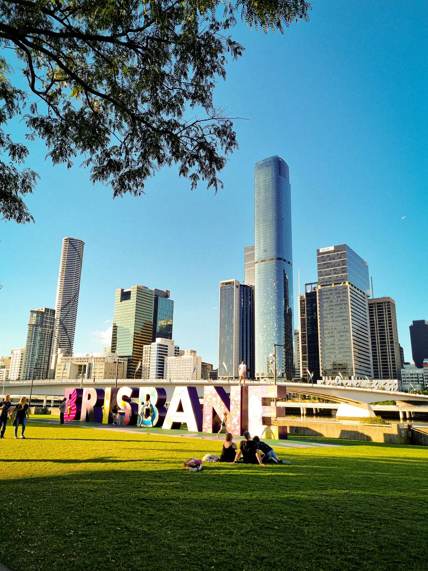 Large Brisbane sign on green grass with the city skyline behind it