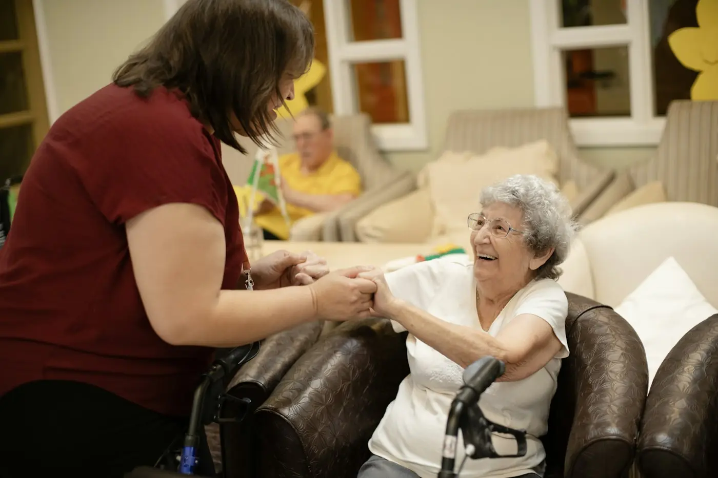 Support worker holding hands with a smiling older woman who is seated