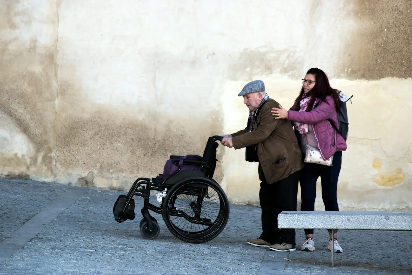 A young woman helping an older man with his wheelchair outdoors